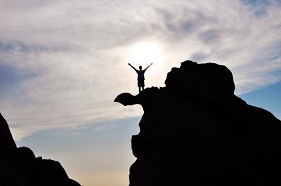 Silhouette d'une personne qui lève les bras au ciel en haut d'un rocher
