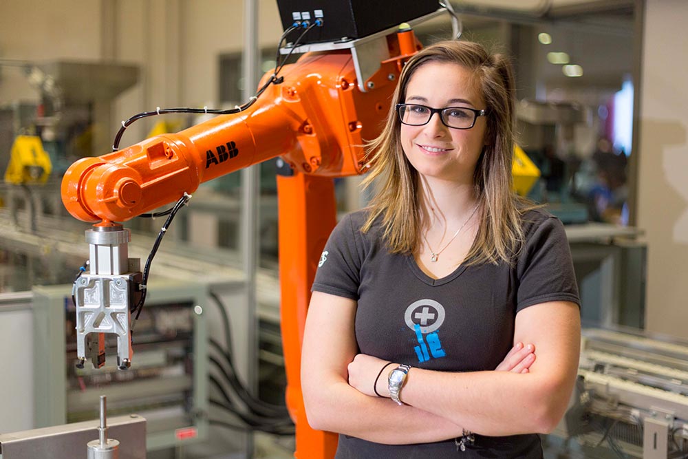 Une étudiante en génie de la production automatisée de l'ÉTS devant une cellule robotisée. e de la production automatisée