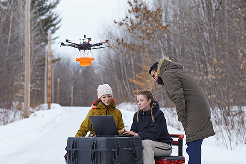 Three people sitting outdoors doing research with a drone