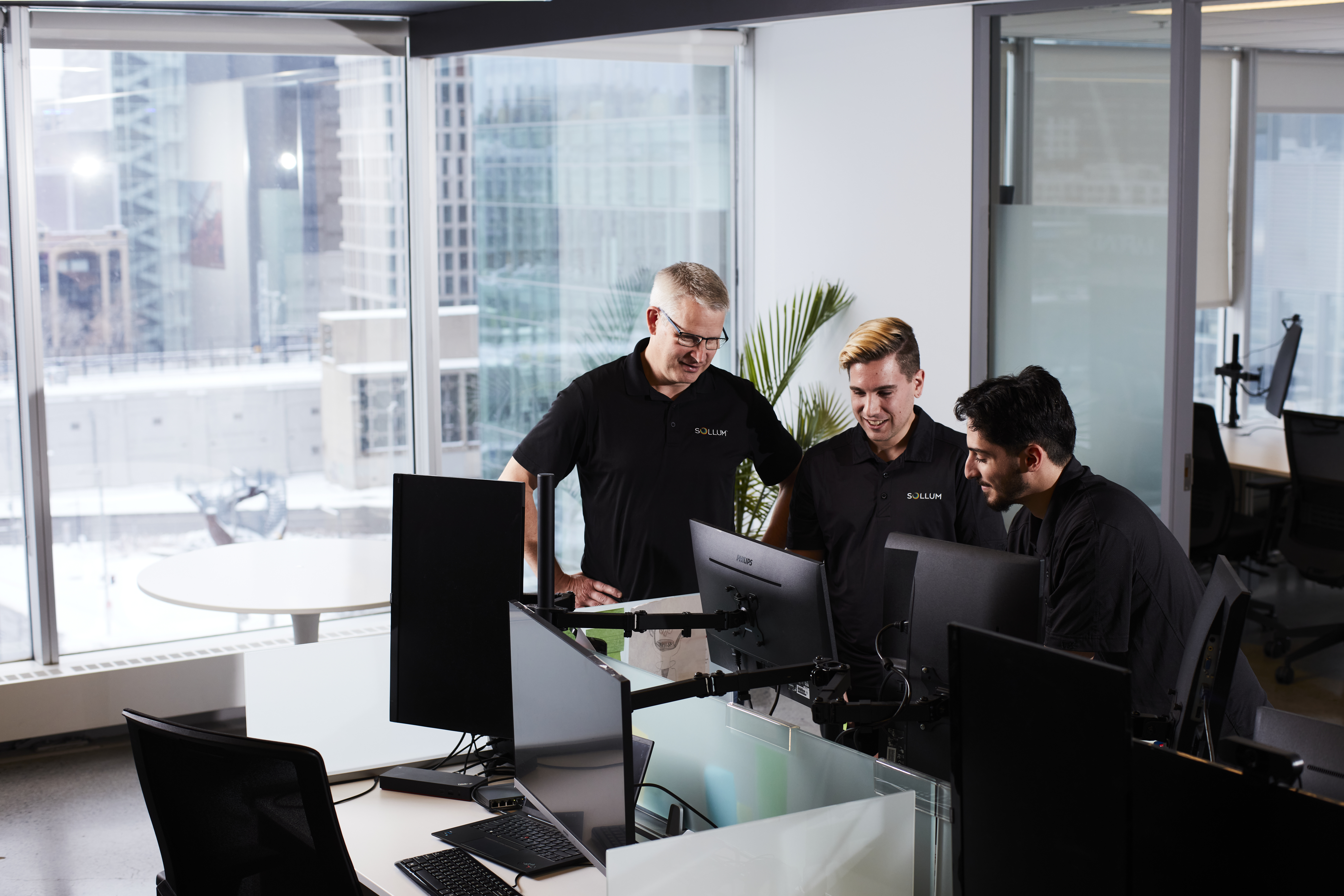 Three professionals exchange ideas around several computers in a modern, collaborative work environment.