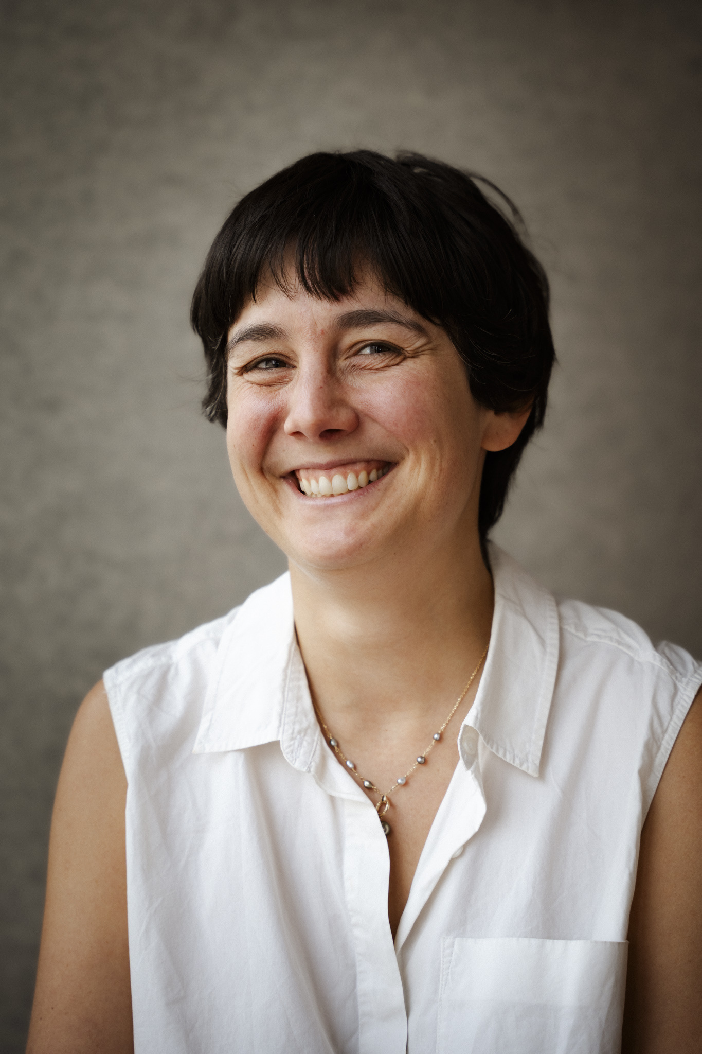 Portrait d'une personne souriante, vêtue d'une chemise blanche, dégageant une attitude amicale et accessible.