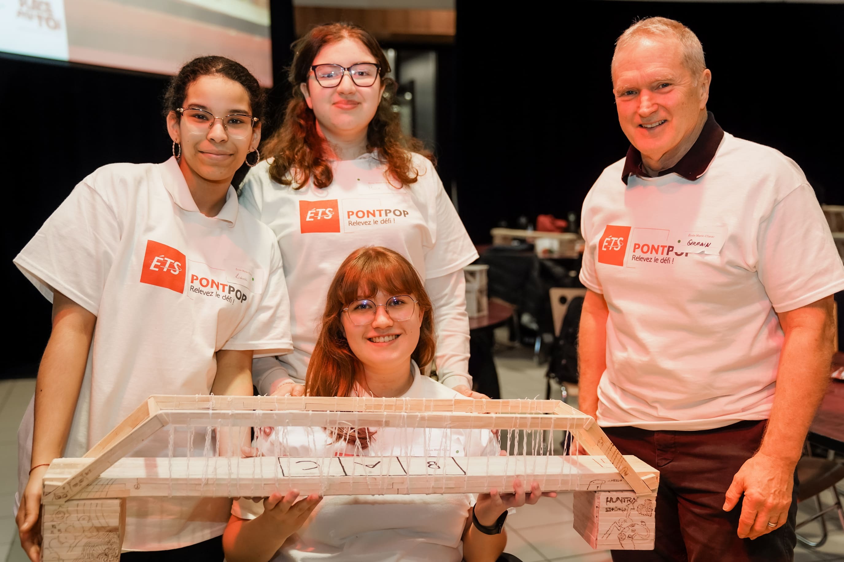 Quatre participants posent fièrement avec leur projet de pont lors d'un événement à l'ÉTS, illustrant l'innovation en ingénierie.