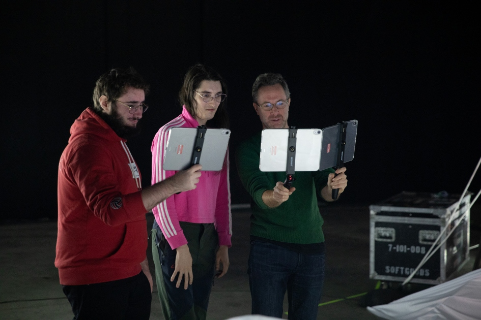 Trois personnes concentrées, tenant des tablettes, explorent un projet technologique dans un environnement sombre et moderne.