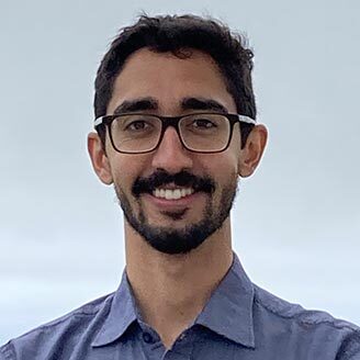 Jeune homme souriant, portant des lunettes et une chemise bleue, associé à l'innovation en technologie.