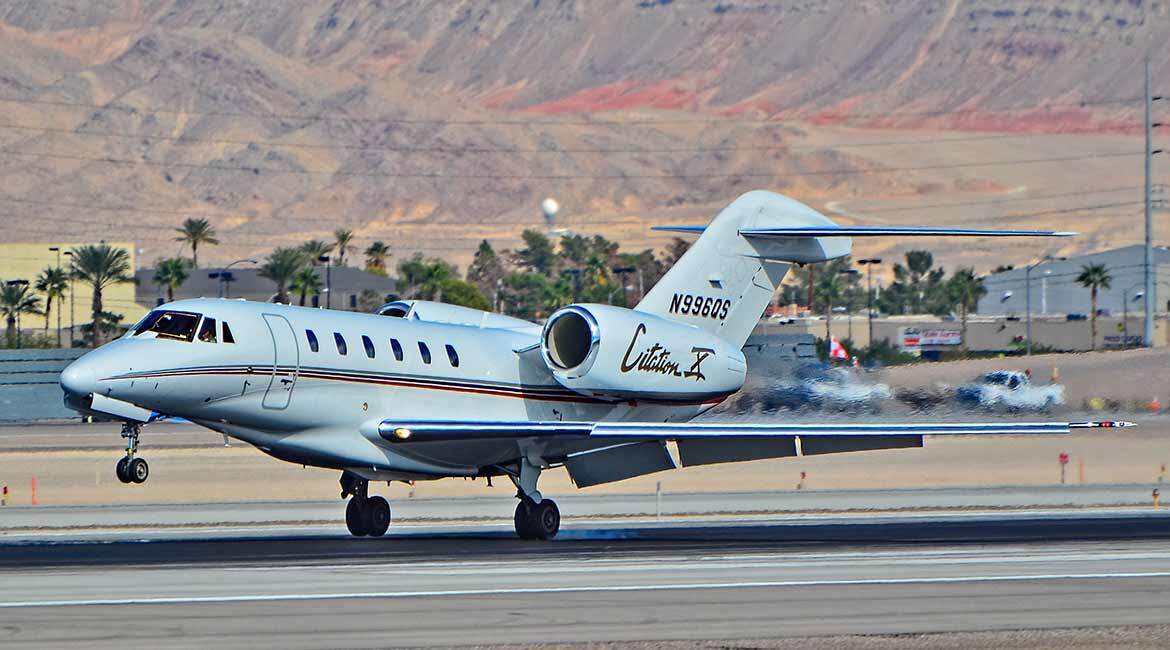 Jet privé Citation X à l'atterrissage, avec un arrière-plan montagneux.