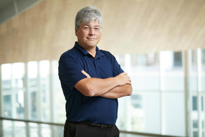Confident professional stands with arms crossed in a modern university building.