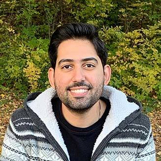 Smiling individual outdoors, wearing a sweater, representing university technology community.