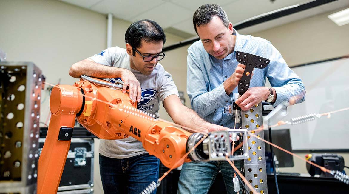 Deux ingénieurs travaillent sur un bras robotique en laboratoire.