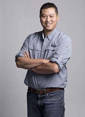 Confident professional in a buttoned shirt and jeans, arms crossed, embodying tech academia's blend of casual and expert.