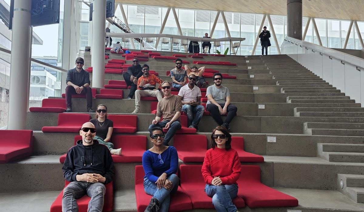 Groupe d'étudiants assis sur des marches modernes, échangeant et profitant de l'espace convivial dans un environnement universitaire.