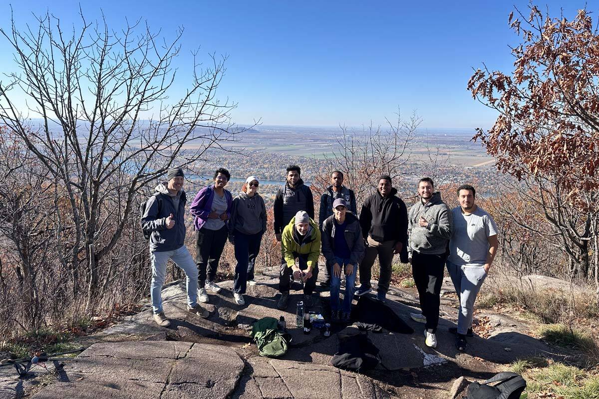Groupe d’étudiants profitant d'une randonnée en montagne, avec une vue panoramique sur la vallée et un ciel dégagé.