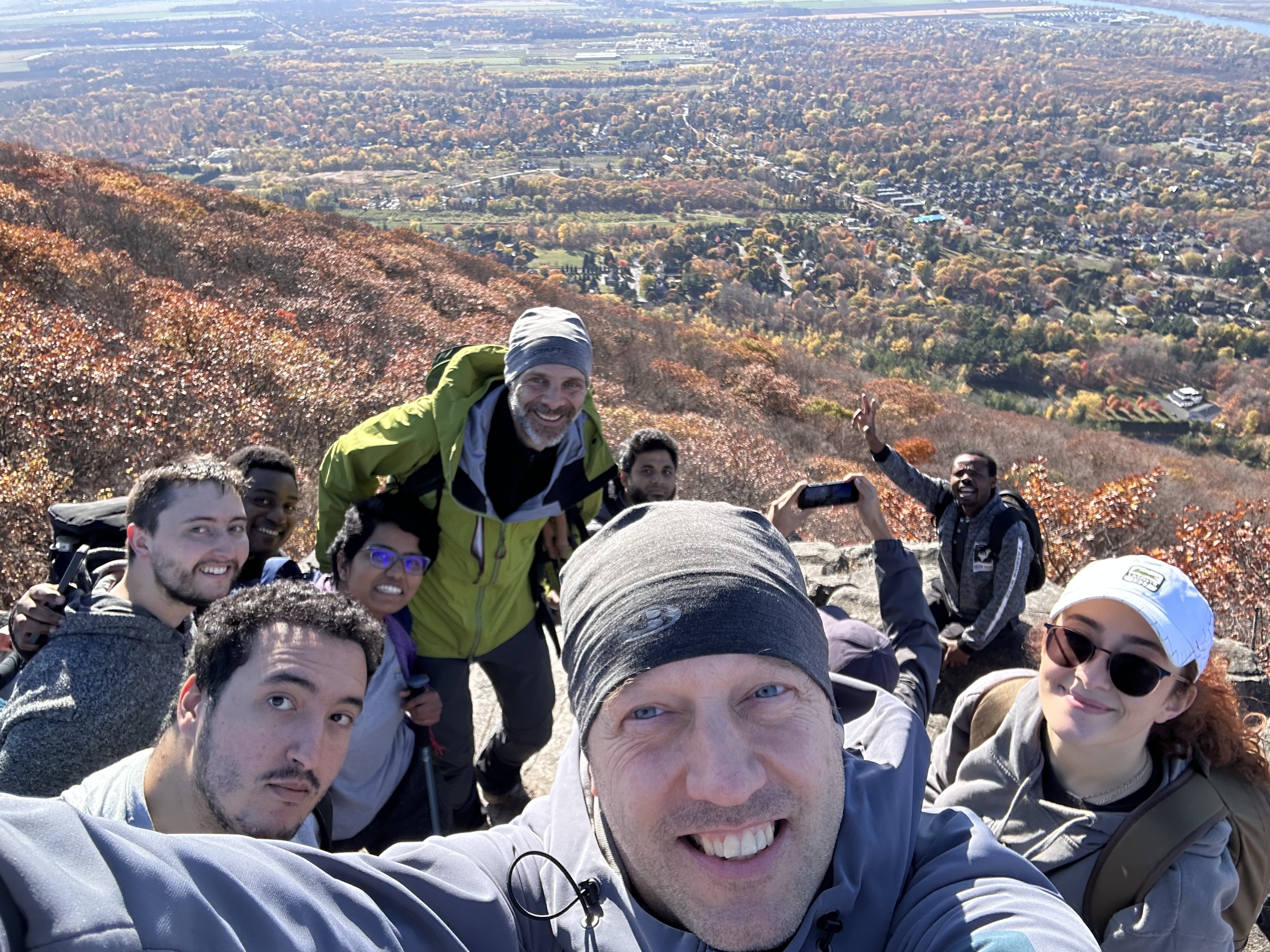Groupe joyeux au sommet d'une montagne, entouré de feuillage automnal vibrant, profitant de la vue panoramique.