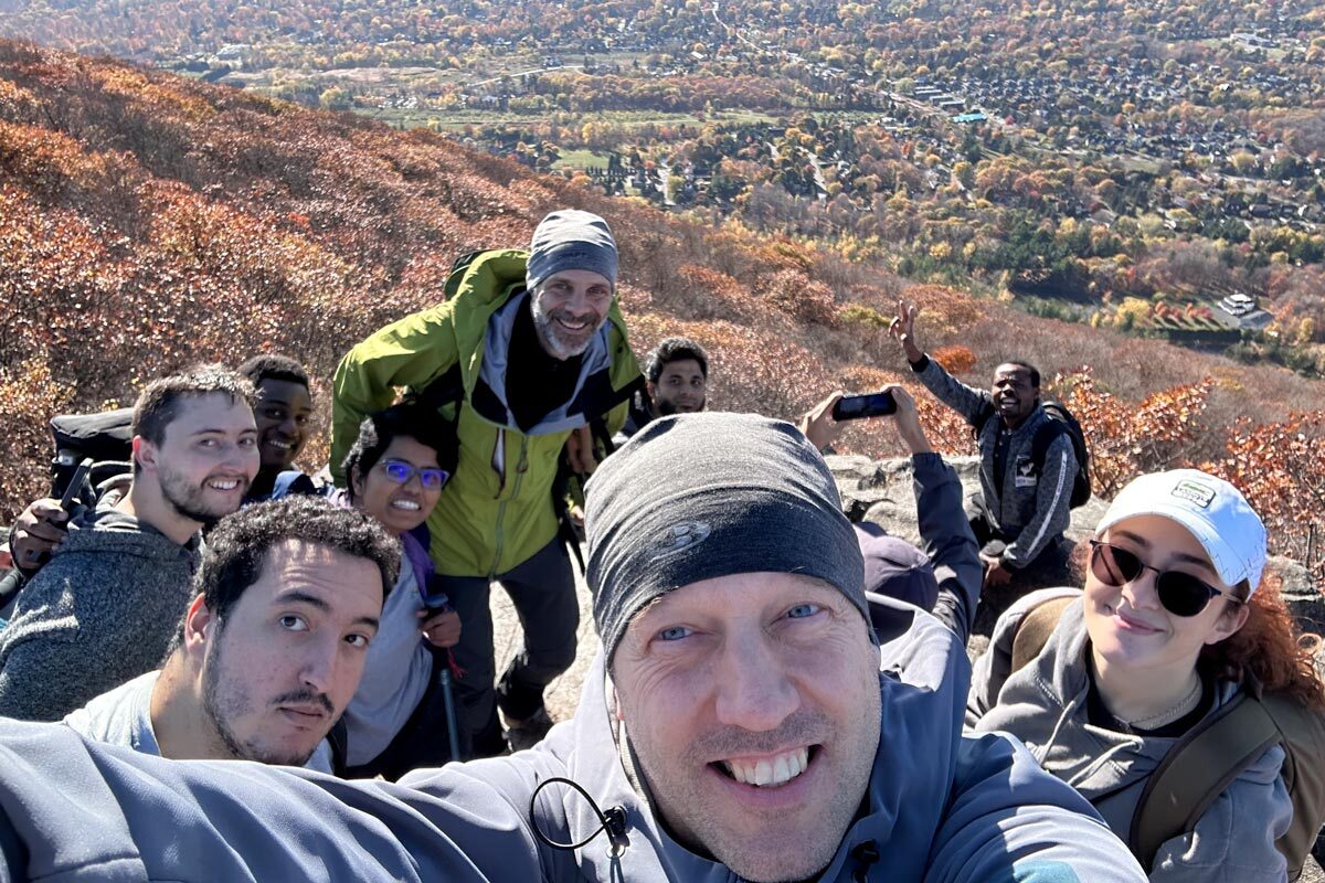 Groupe joyeux au sommet d'une montagne, entouré de feuillage automnal vibrant, profitant de la vue panoramique.