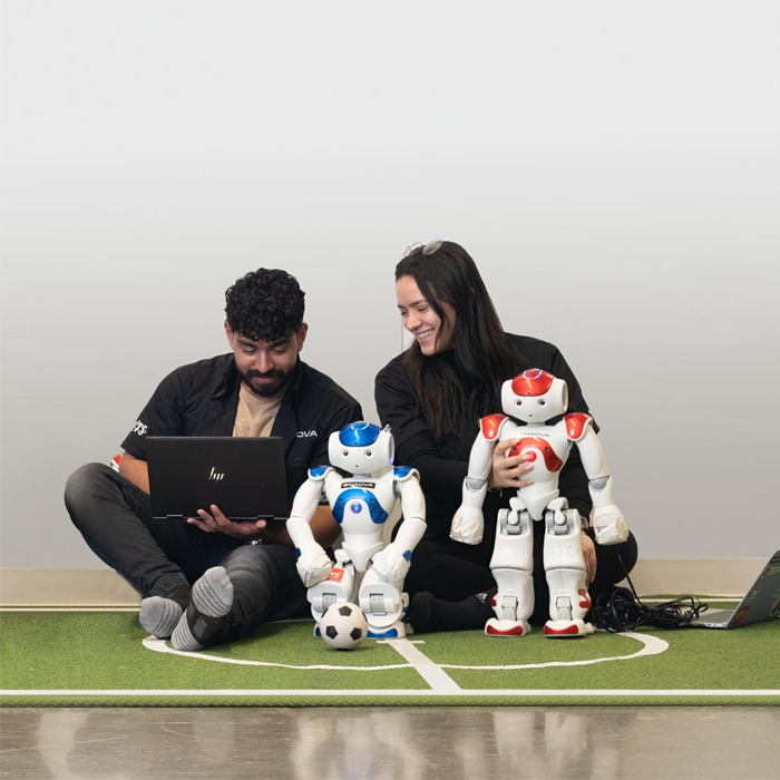 Des étudiants interagissent avec des robots humanoïdes sur un terrain de football miniature, explorant la technologie et l'innovation.