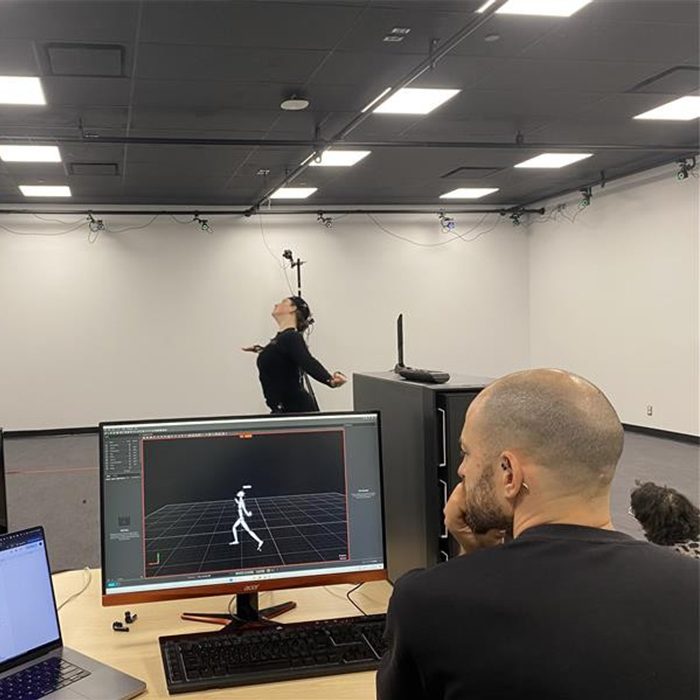 Une chercheuse réalise des mouvements dans un espace de capture de mouvement, tandis qu'un homme analyse les données sur un ordinateur.
