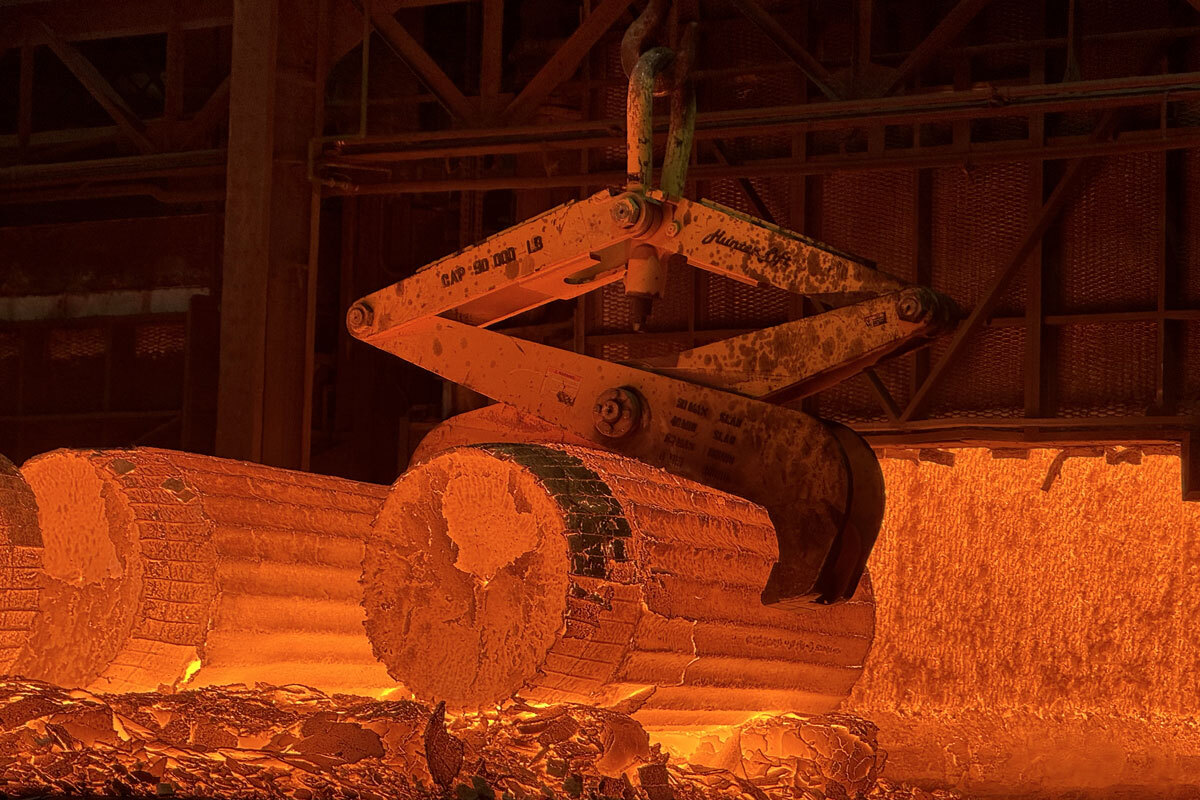 Une grue spécialisée manipule des lingots métalliques incandescents dans un environnement industriel impressionnant.