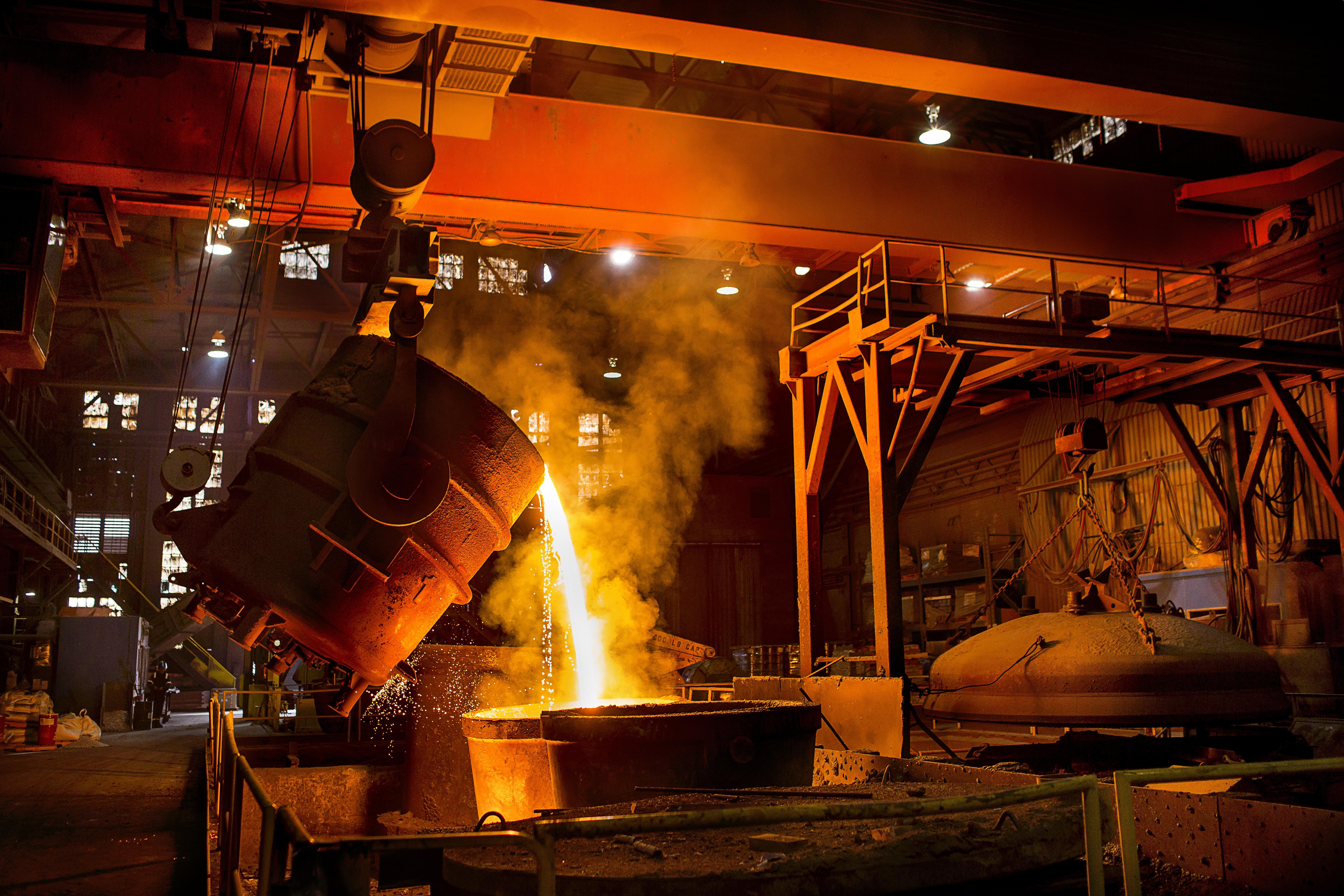 A large furnace pours molten metal into a mold, illuminating the industrial environment with fiery orange hues.
