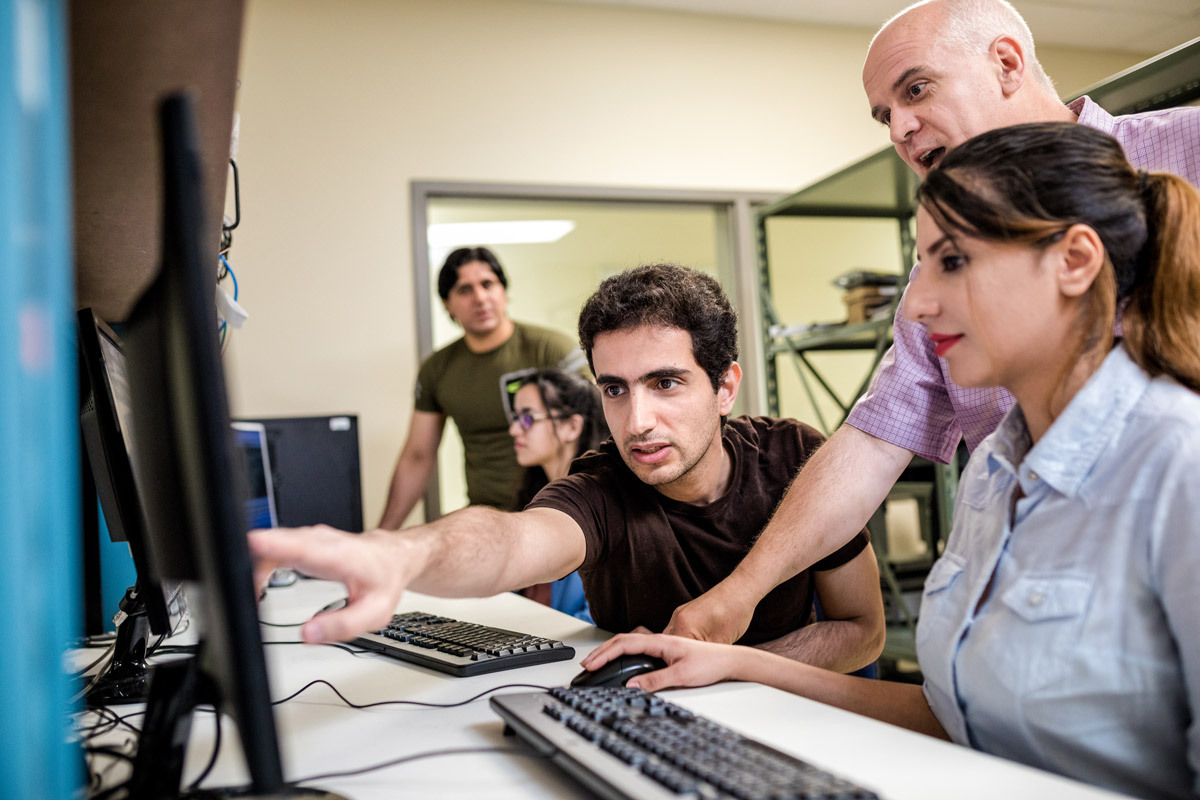 Des étudiants travaillent ensemble sur un projet, échangeant des idées et des conseils devant des ordinateurs. Collaboration dynamique et apprentissage.