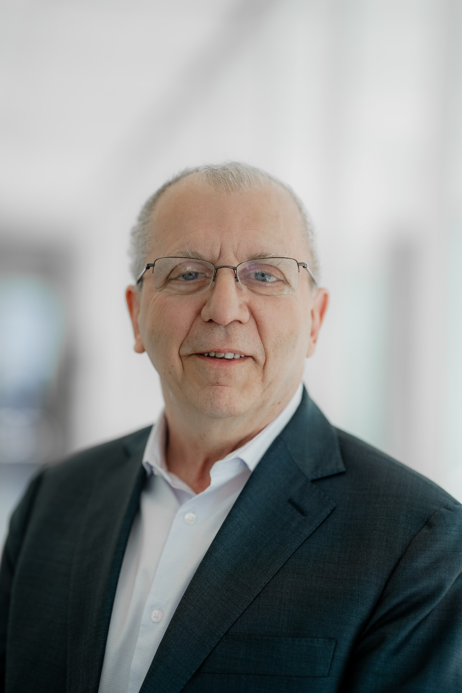 Portrait d'un homme souriant, portant une tenue professionnelle, dans un environnement lumineux et moderne.