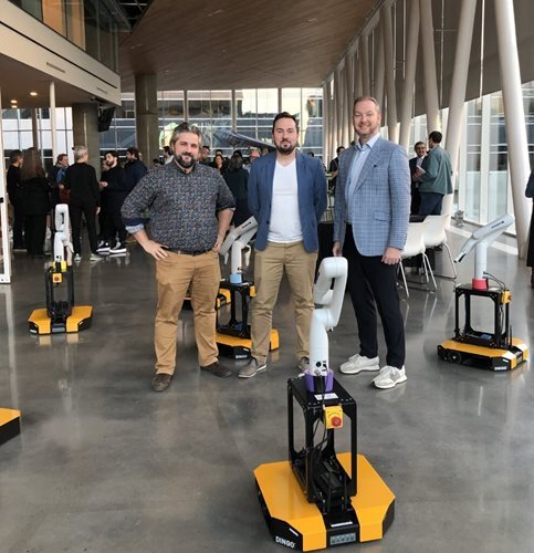 Three professionals with robotics equipment at a university technology event.