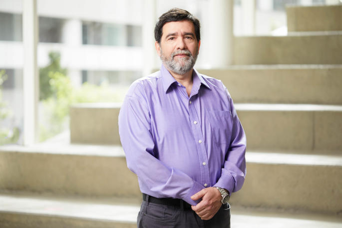Confident professional in purple shirt poses at a modern university campus.