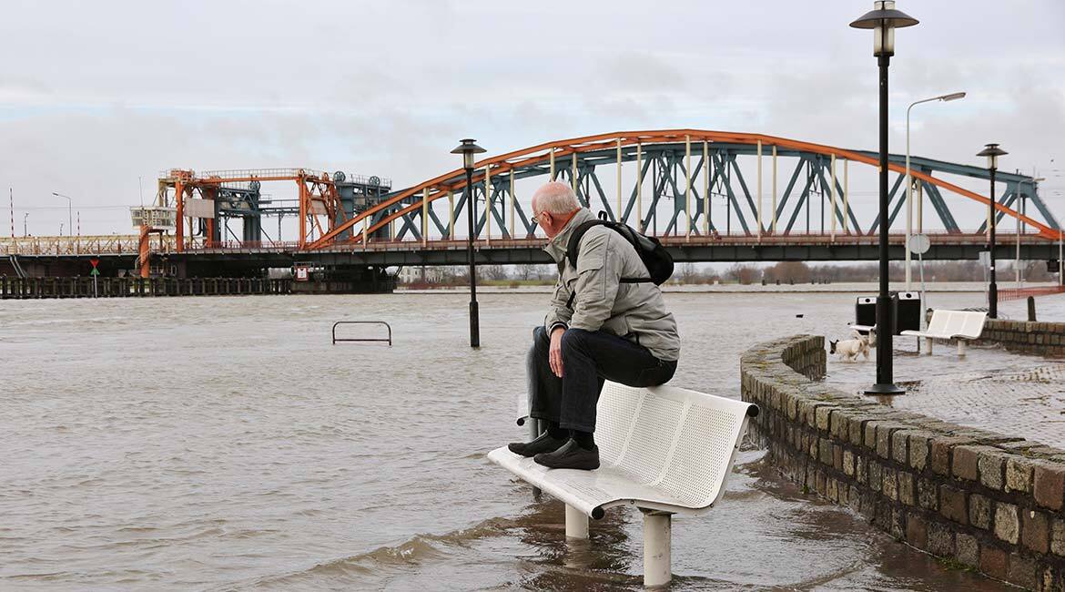 Homme assis sur un banc, inondation devant un pont.