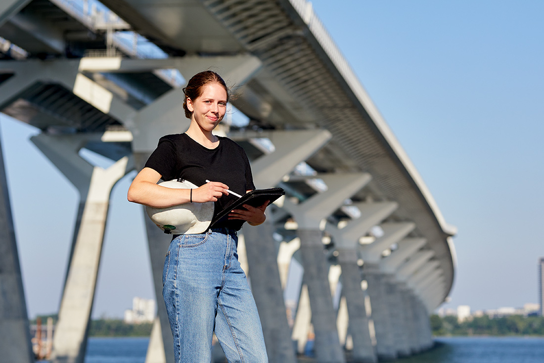 Étudiante ingénieure consultant une tablette près d'un pont moderne.
