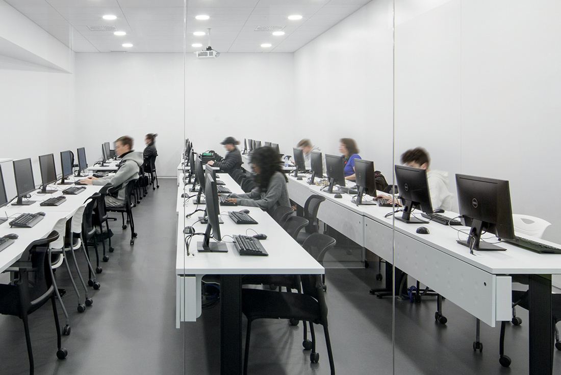 Salle informatique moderne avec étudiants concentrés sur des ordinateurs.