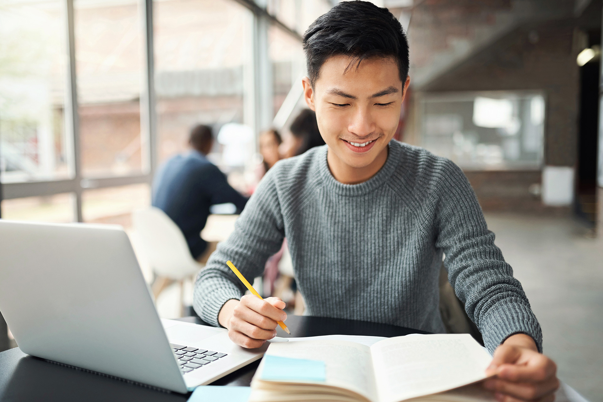 Étudiant souriant travaillant avec un ordinateur portable et prenant des notes.