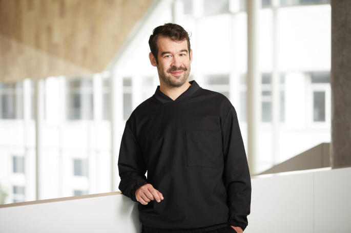 Confident faculty member stands casually in a modern university setting, embodying innovative technology education.