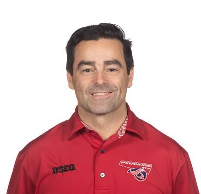 Professeur en technologie, chemise rouge avec logo d'équipe, souriant, fond blanc.
