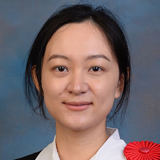 Portrait d'une professionnelle avec un insigne rouge, souriante, arrière-plan uni. Représente l'expertise en technologie.