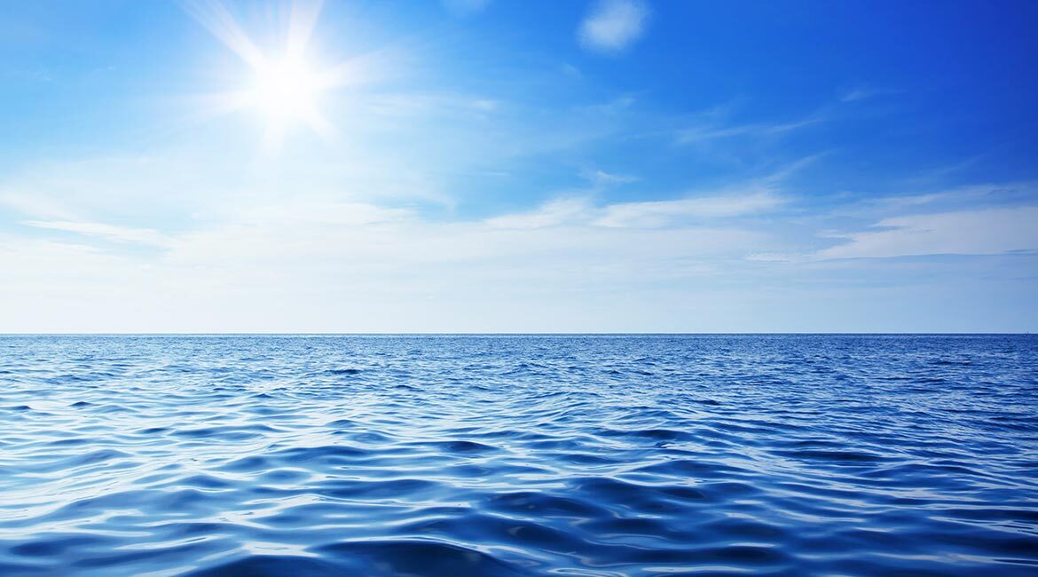 Horizon marin sous un ciel bleu avec soleil éclatant.