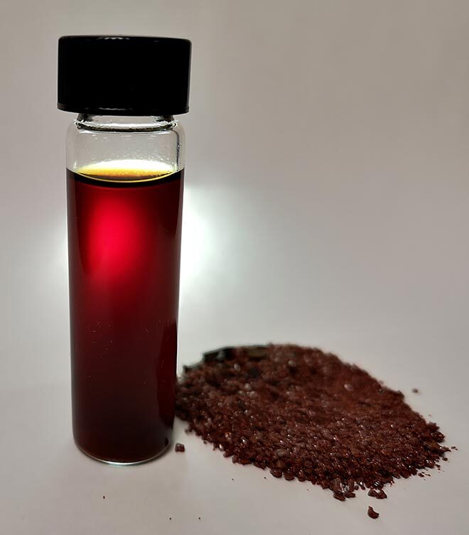 Échantillon de liquide rougeâtre dans un flacon, avec granulés similaires dispersés à côté.