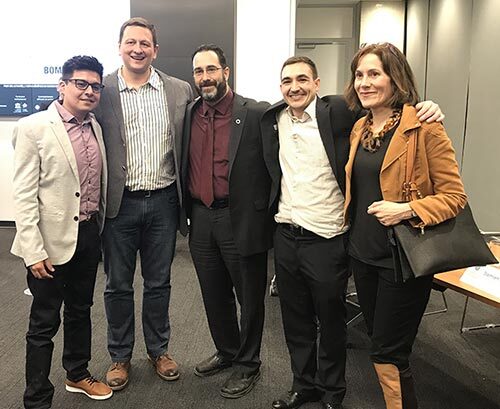 Groupe de cinq professionnels souriants, réunis dans un cadre universitaire.