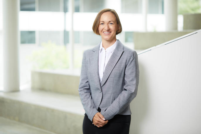 Professional educator in business attire at a university technology center, smiling confidently.