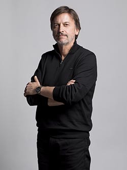 Homme en polo noir, bras croisés, sérieux, évoquant professionnalisme et expérience.