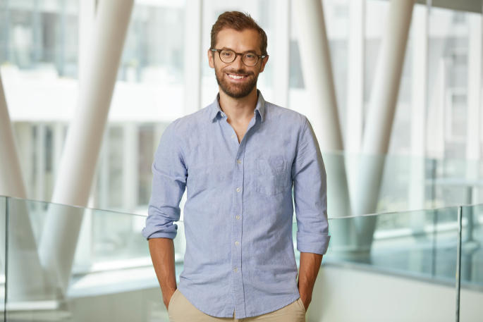 Homme souriant en chemise bleue, représentatif de l'ambiance dynamique et moderne d'une université technologique.