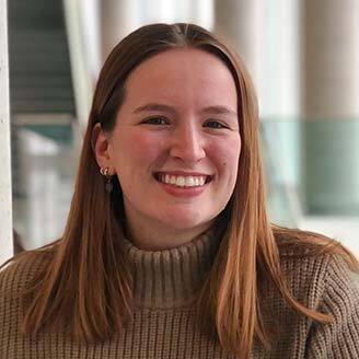 Étudiante souriante en pull beige, dans un cadre universitaire, incarne la joie d'apprendre.