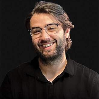 Faculty member in tech, smiling, with glasses and beard, dressed in black.