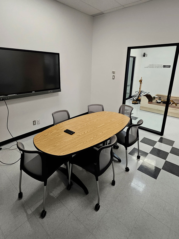 A modern conference room featuring a large oval table, rolling chairs, and a wall-mounted display, ideal for collaborative meetings.