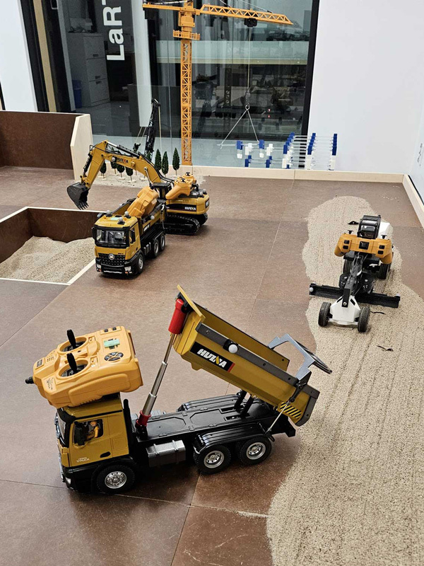 A miniature construction setup featuring remote-controlled trucks and machinery on a sandy terrain, showcasing engineering and technology.