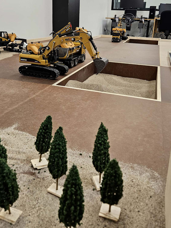 A miniature construction site featuring scaled models of heavy machinery and realistic landscaping elements for educational purposes.