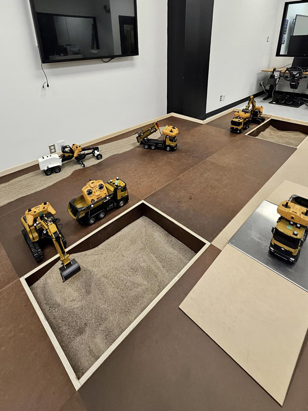 A simulation area featuring remote-controlled construction vehicles interacting with sand and terrain for educational purposes.