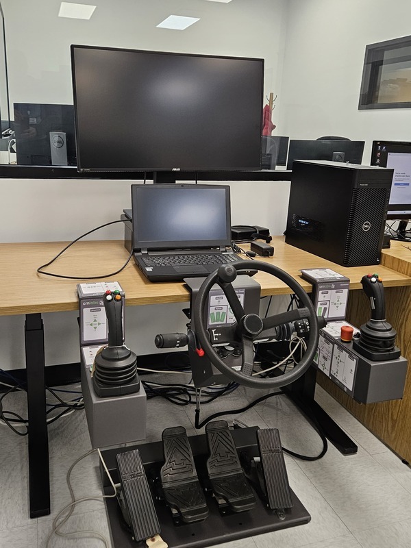 A simulation setup featuring a steering wheel, joysticks, pedals, and dual monitors for advanced technology training.