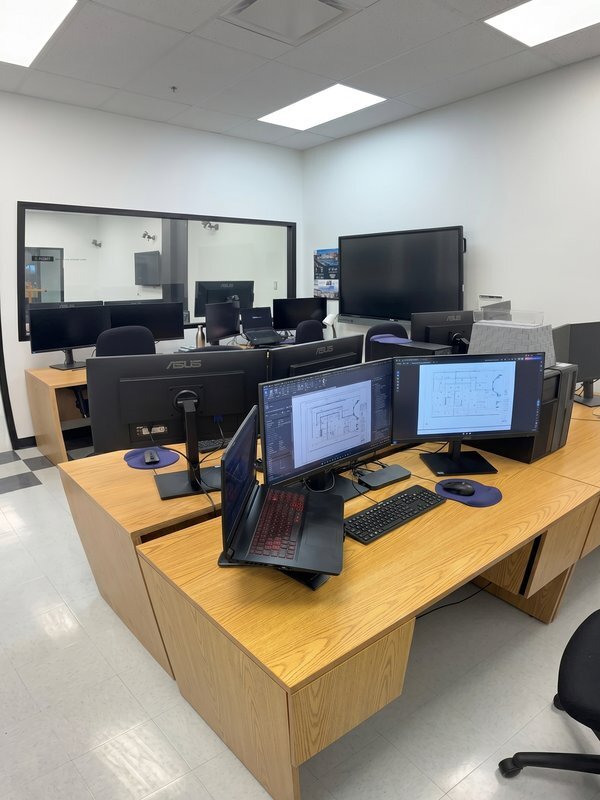 A modern technology workspace featuring multiple computers, large monitors, and collaborative areas for students and professionals.