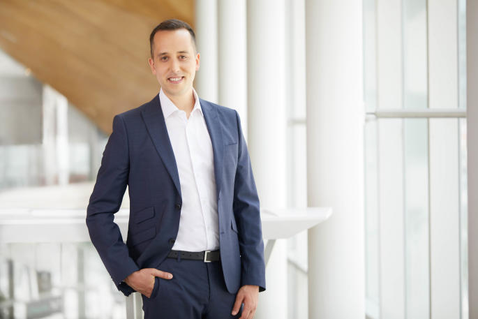 Homme en costume souriant, professionnel dans un cadre universitaire moderne.