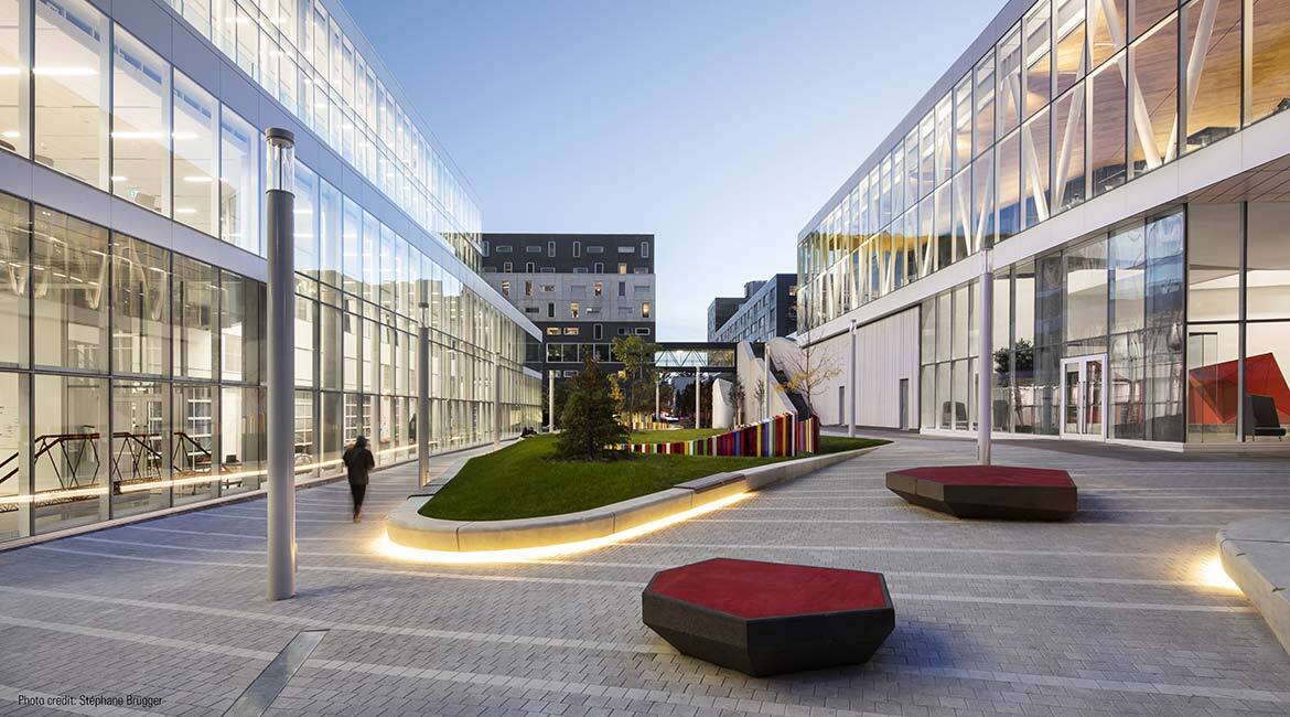 Campus moderne avec bâtiments vitrés, espace vert et éclairage extérieur.