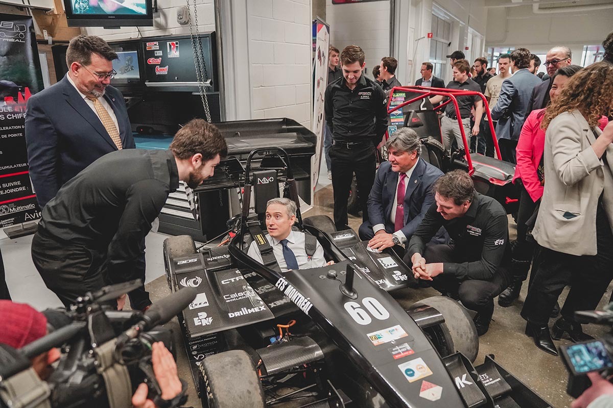 Visite officielle dans un atelier de course avec discussions techniques autour d'une voiture de formule.