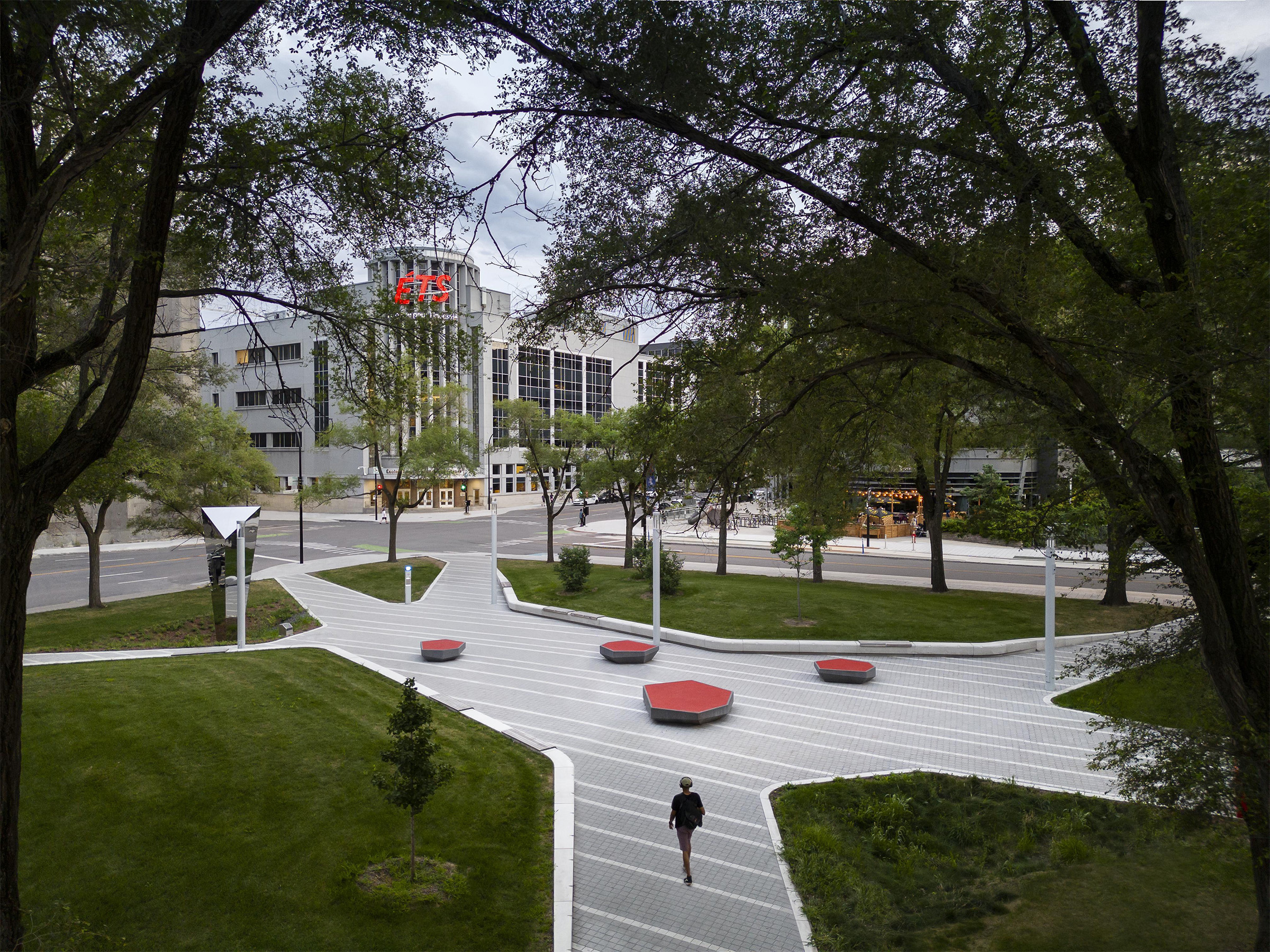 Campus verdoyant avec zones de repos, chemins pavés et bâtiment au logo rouge et blanc.